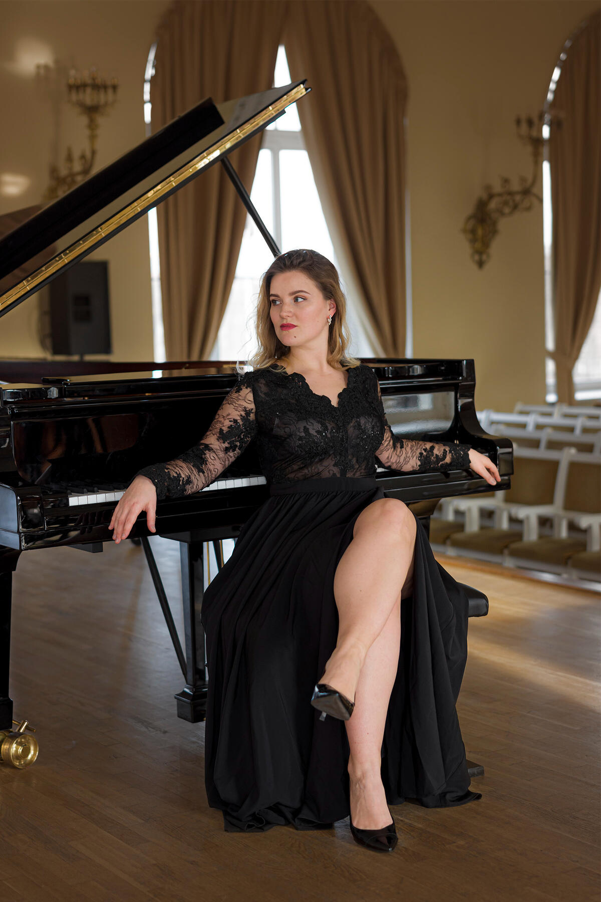 Asmeninė muzikantės fotosesija Šviesiaplaukė mergina su ilga juoda suknele pozuoja prie pianino. Asmeninė fotosesija.