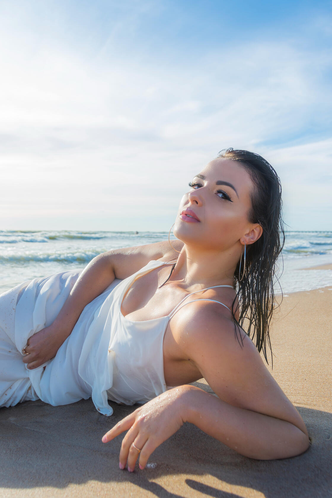 Jauna moteris balta suknele pajūryje sėdi bangose – vasariška fotosesija prie jūros. Profesionali fotosesija gamtoje.