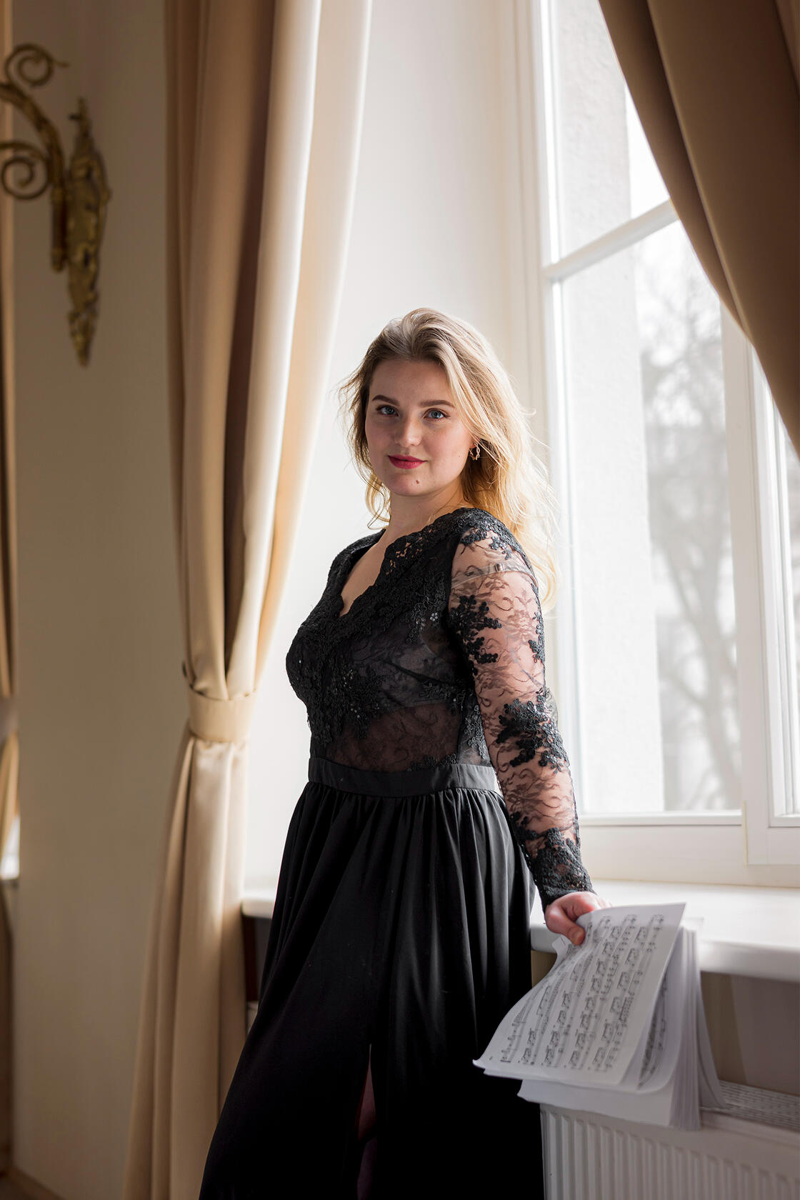 Muzikantė pozuoja su natomis rankoje. Vidutinio plano kadras