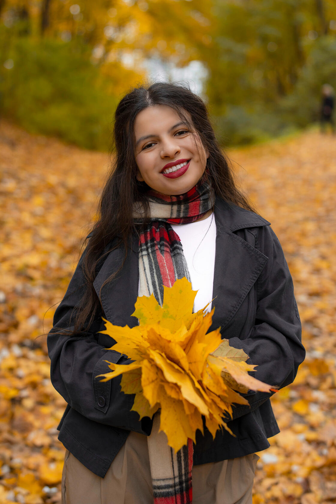 Tamsiaplaukė mergina pozuoja tarp geltonų lapų