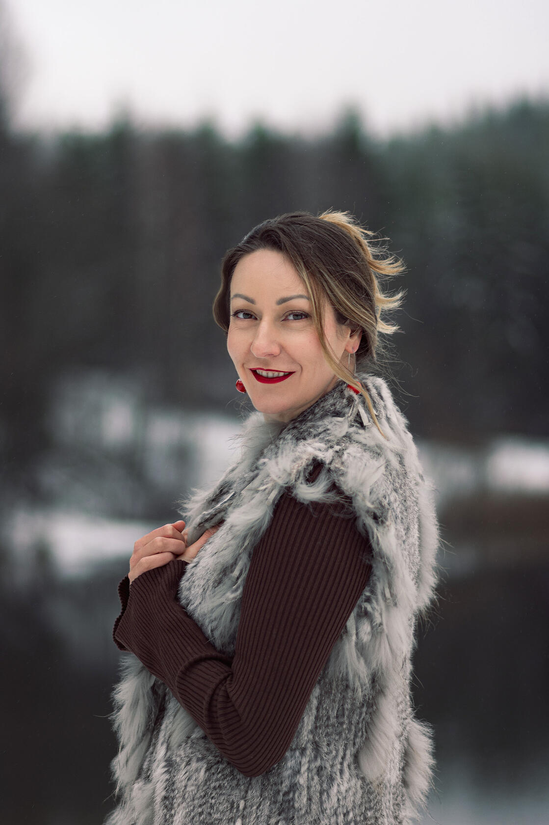 Moteris raudonomis lūpomis apsivilkusi kailinius žiūri į objektyvą