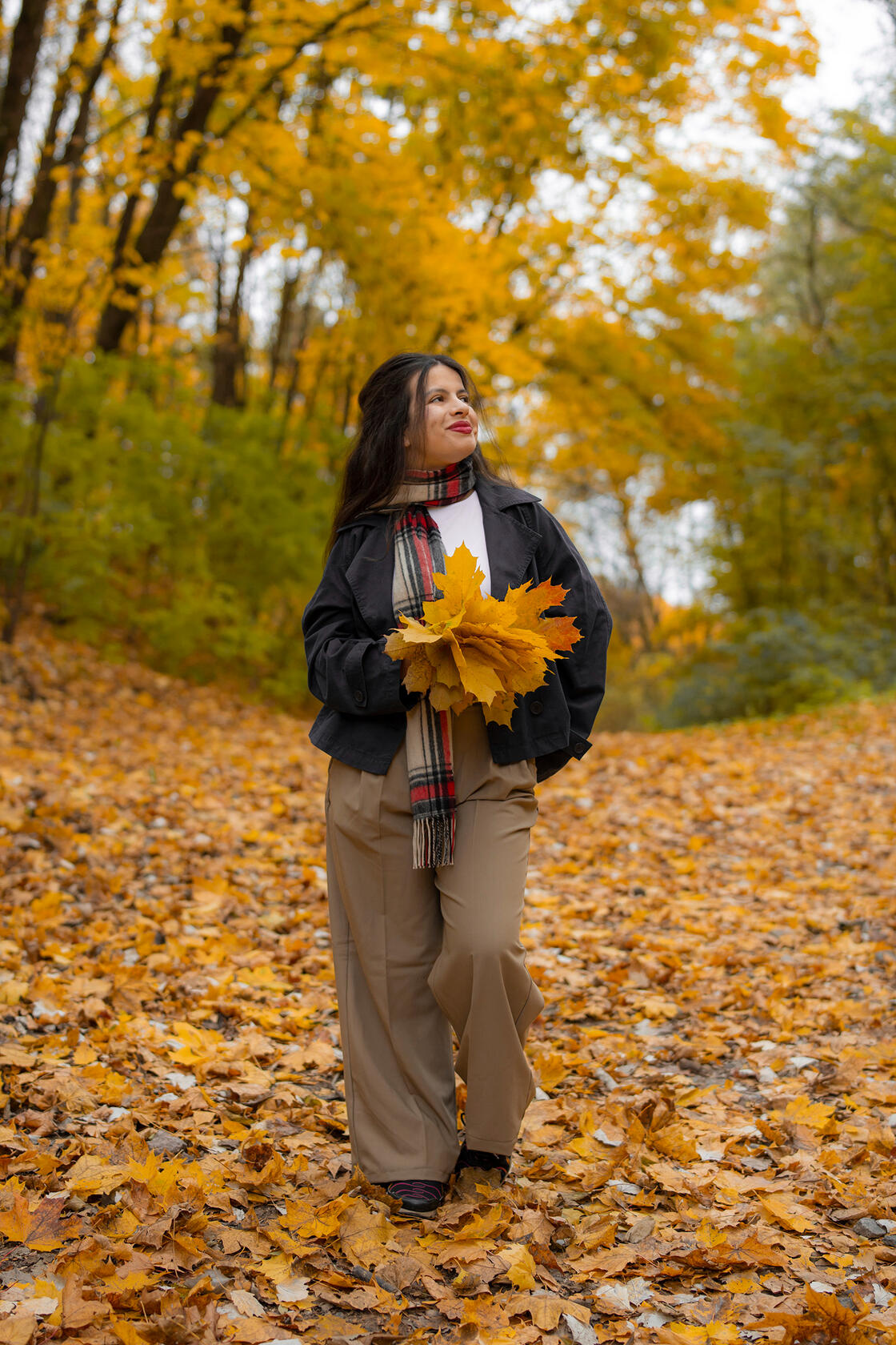 Tamsiaplaukė mergina pozuoja tarp geltonų lapų