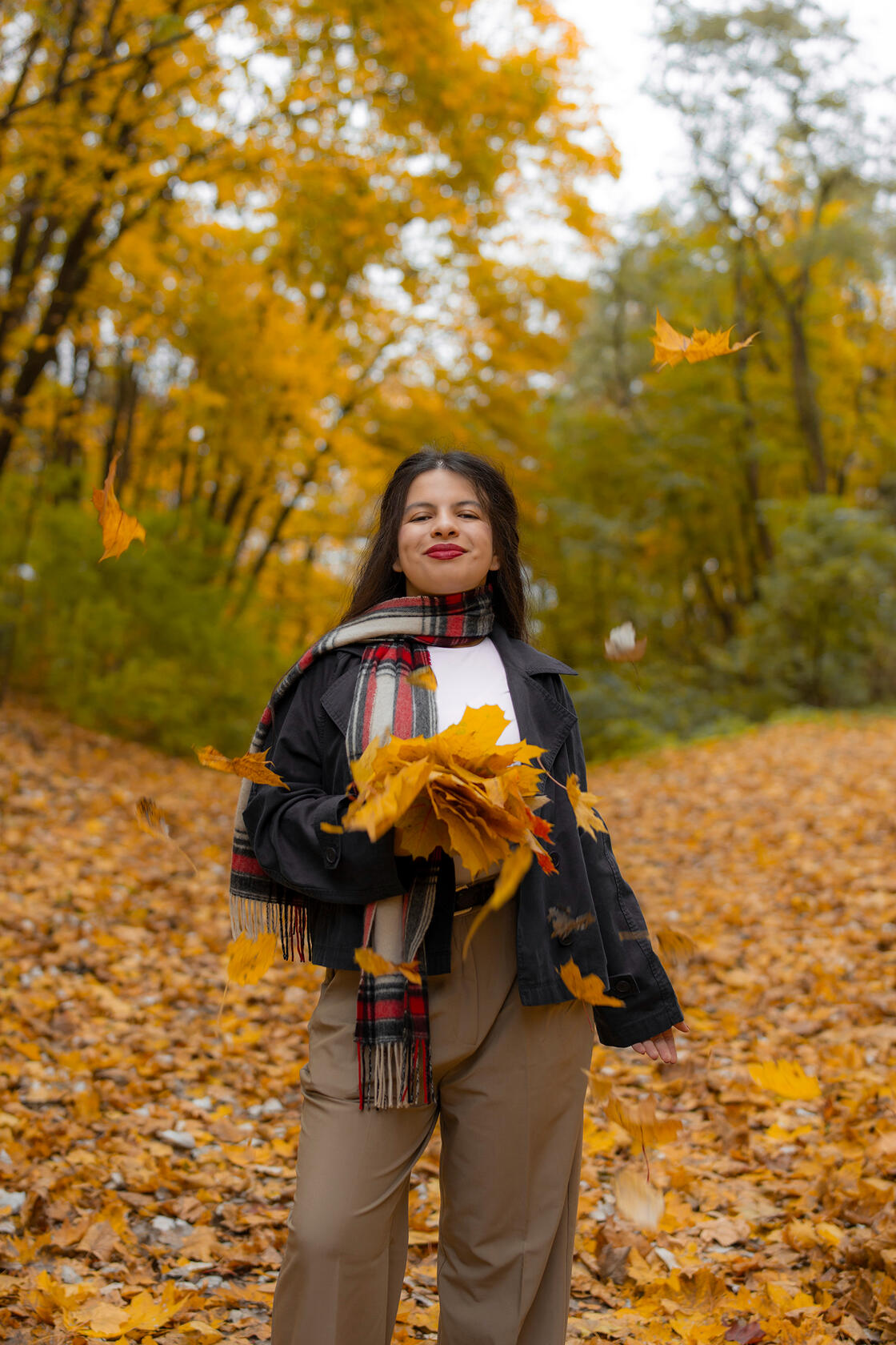 Tamsiaplaukė mergina pozuoja tarp geltonų lapų