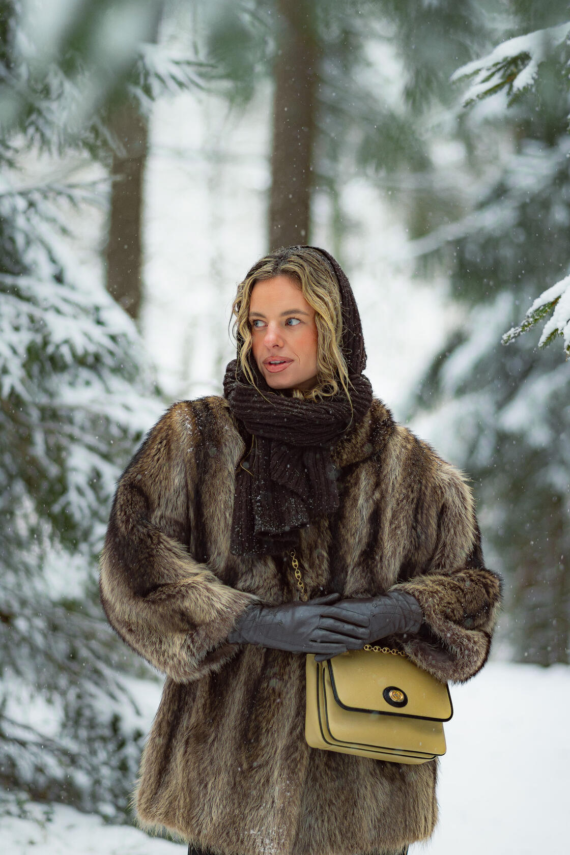 Asmeninė fotosesija Vilniuje, krenta sniegas, mergina apsirengusi kailiniais šaliku ir pirštinėmis žvelgia į šoną