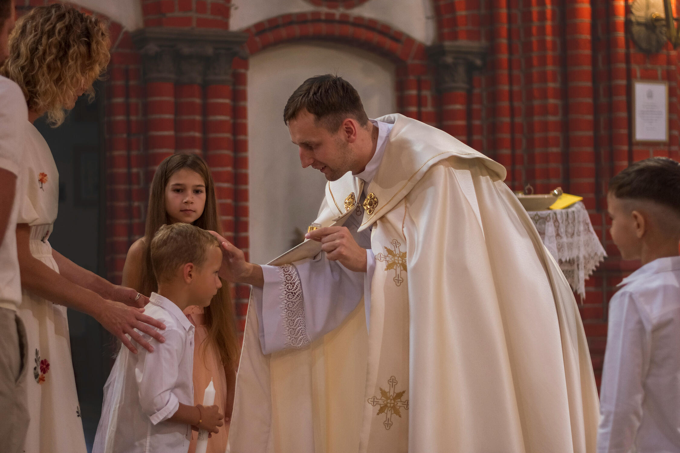 Krikštynų fotosesija Krikštynų fotografija, kunigas laimina vaiką