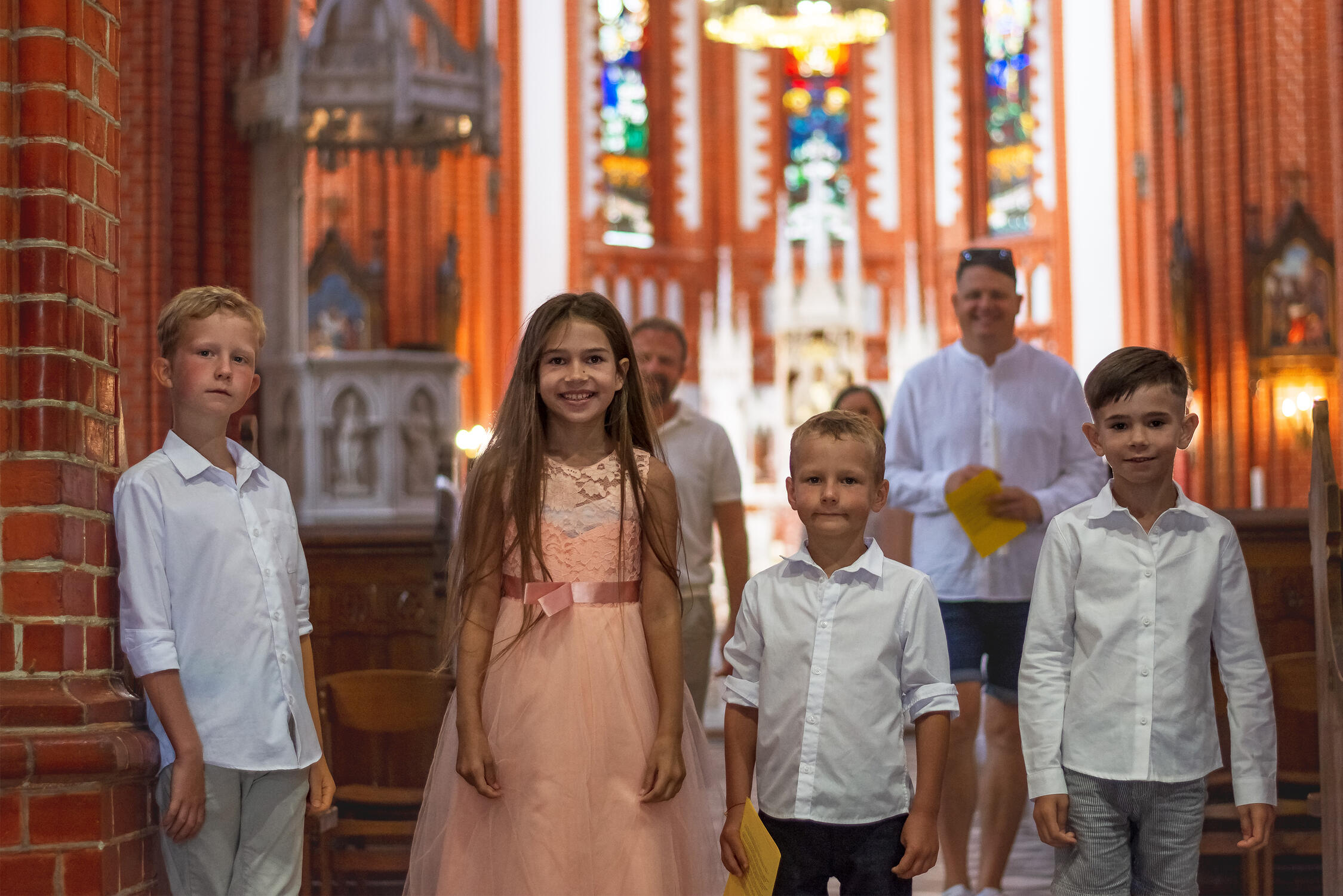 Laimingi vaikai pozuoja krikštynų fotografui, fone bažnyčios altorius