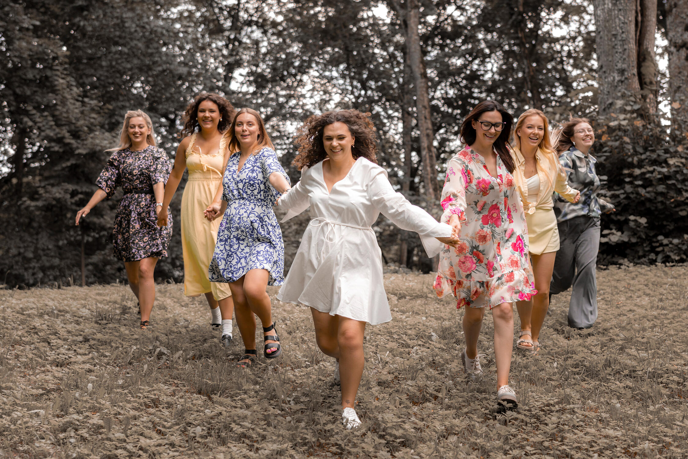 moterys pasipuošusios vasariškomis suknelėmis pozuoja prieš objektyvą, bėga į mergvakario fotografę